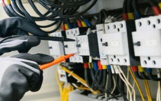 Elektrofachkraft prüft elektrische Anschlüsse und Sicherungen in einem Schaltschrank mit Messspitzen.