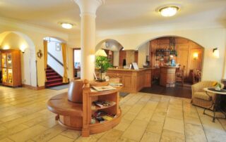 Einladende Lobby des Hotel Alpenglück mit gemütlichem Empfang, stilvollen Möbeln und einer kleinen Leseecke für Hotelgäste.