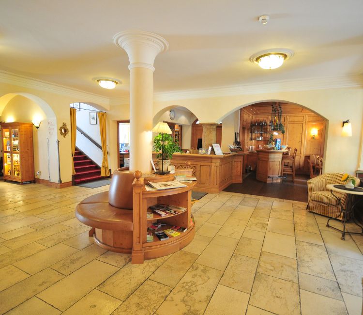 Einladende Lobby des Hotel Alpenglück mit gemütlichem Empfang, stilvollen Möbeln und einer kleinen Leseecke für Hotelgäste.