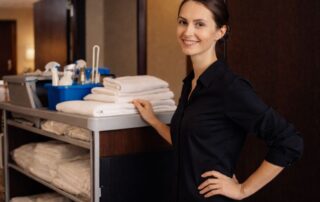 Eine Reinigungskraft im Hotel lächelt vor einem Wagen mit frischen Handtüchern, bereit für ihren Einsatz.