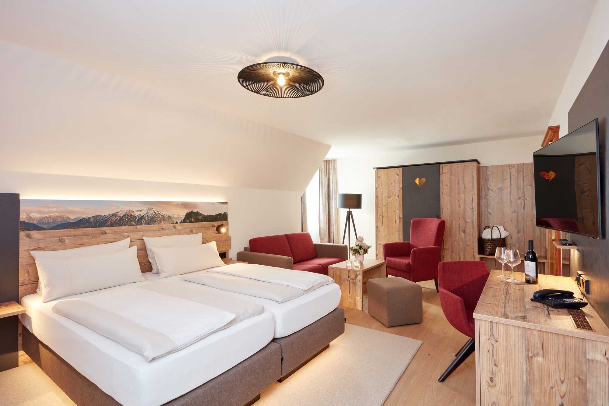 Gemütliches Hotelzimmer im Hotel Alpenglück, ausgestattet mit einem Doppelbett, Sitzbereichen und einem TV, ideal für einen Familienurlaub in den Bergen.