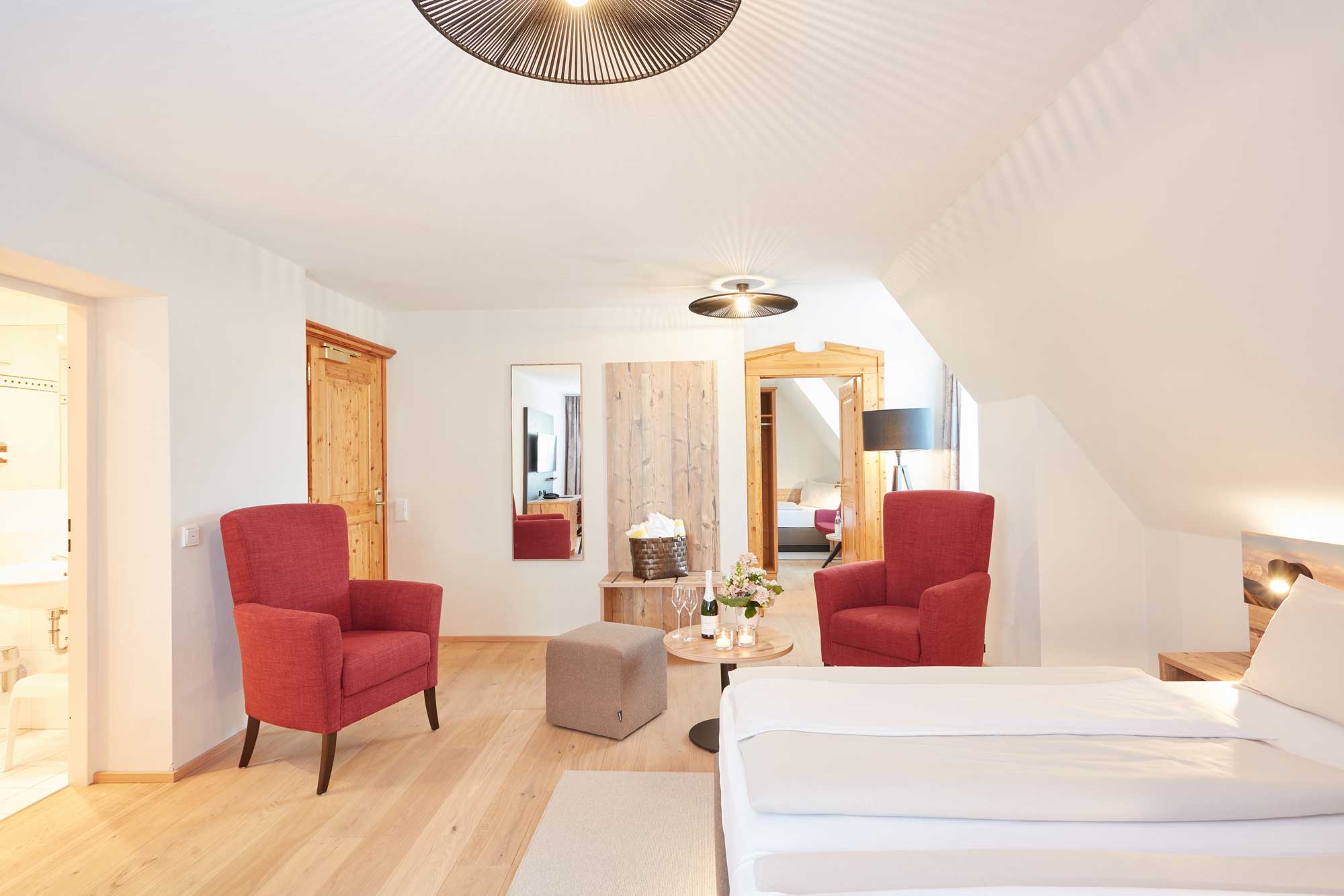 Geräumiges Zimmer im Hotel Alpenglück mit roten Sesseln, Holzdetails und modernem Ambiente für einen erholsamen Familienurlaub.