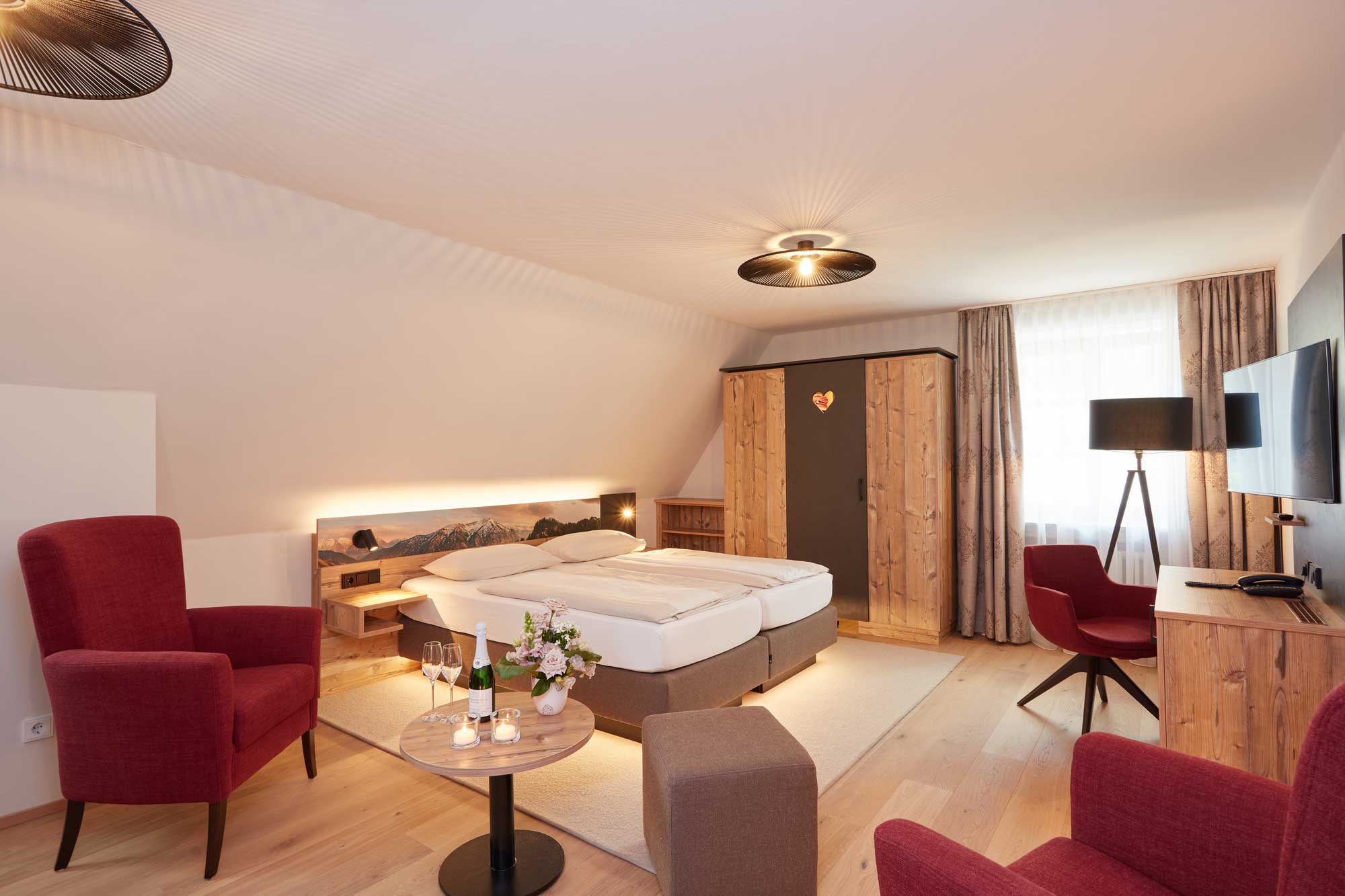 Gemütliches Hotelzimmer im Hotel Alpenglück mit Doppelbett, Sessel und Fernseher, ideal für einen erholsamen Familienurlaub.